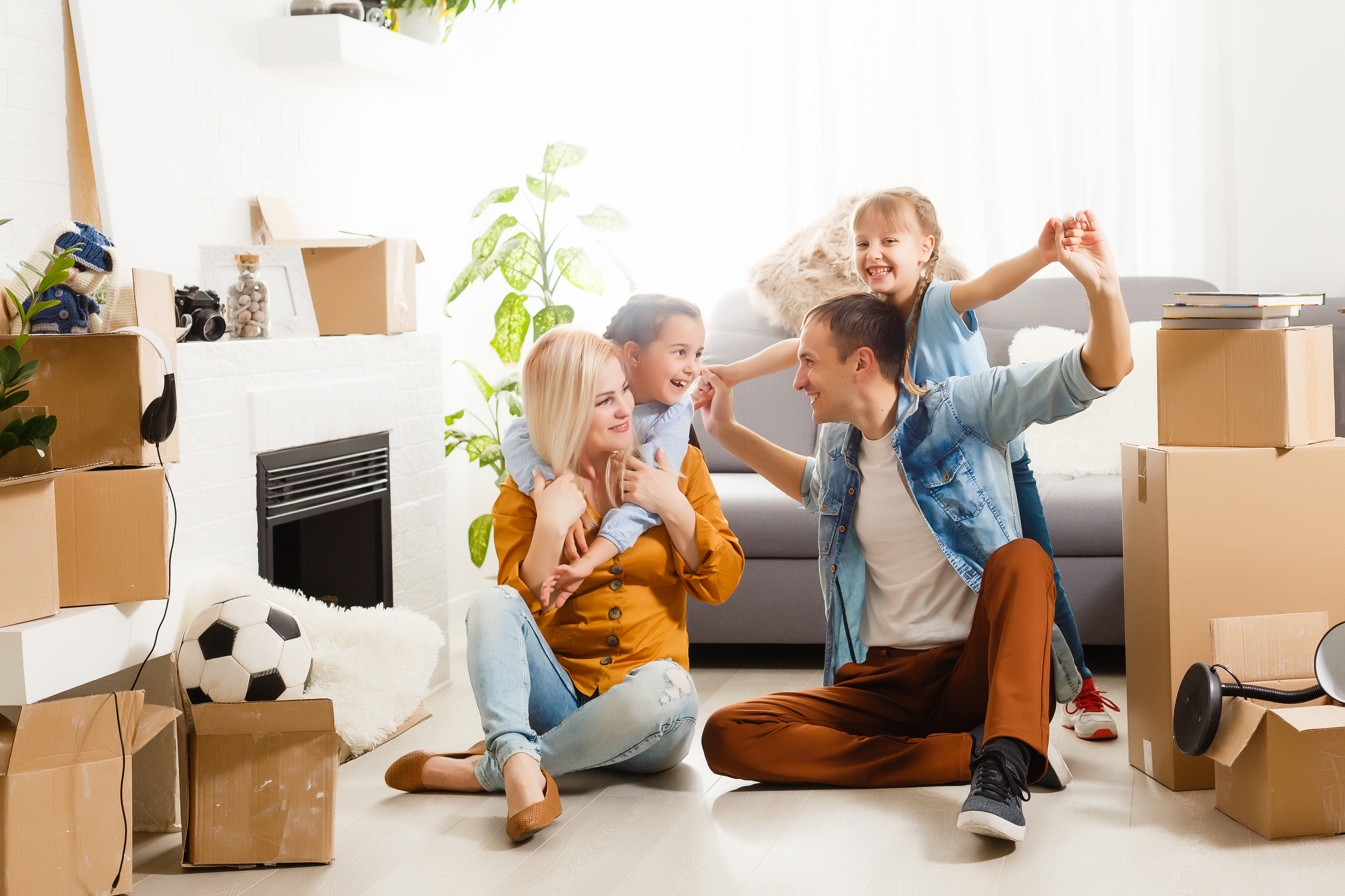 A happy family of four standing sitting together in their home, smiling and playing. They have just received electrical service from an electrical contractior and are satisfied with the quality of work.